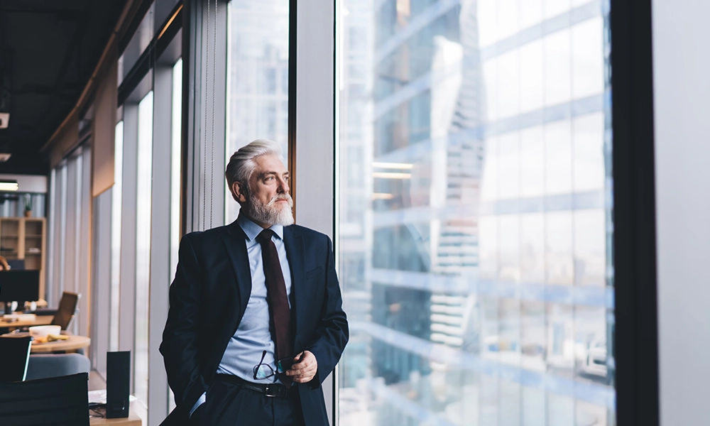 Man stands at a large window in an office building. 